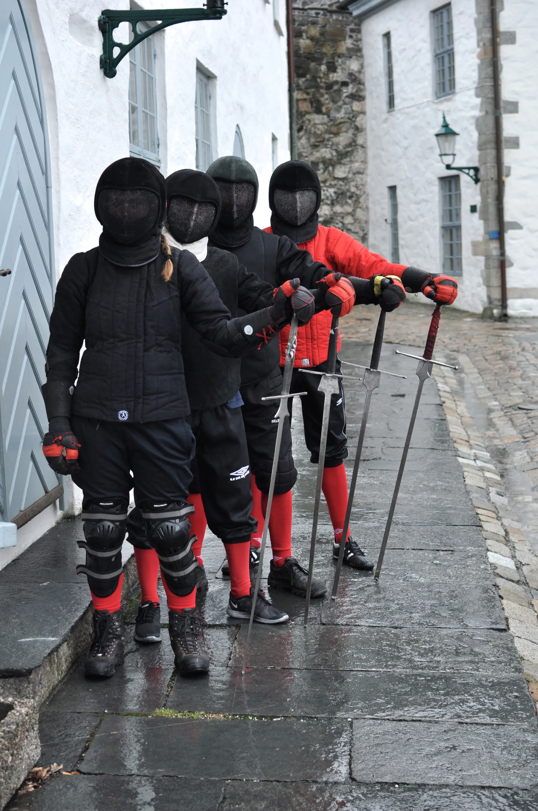 En rekke fektere i masker og røde og svarte jakker venter på tur med sverdene i hånden.