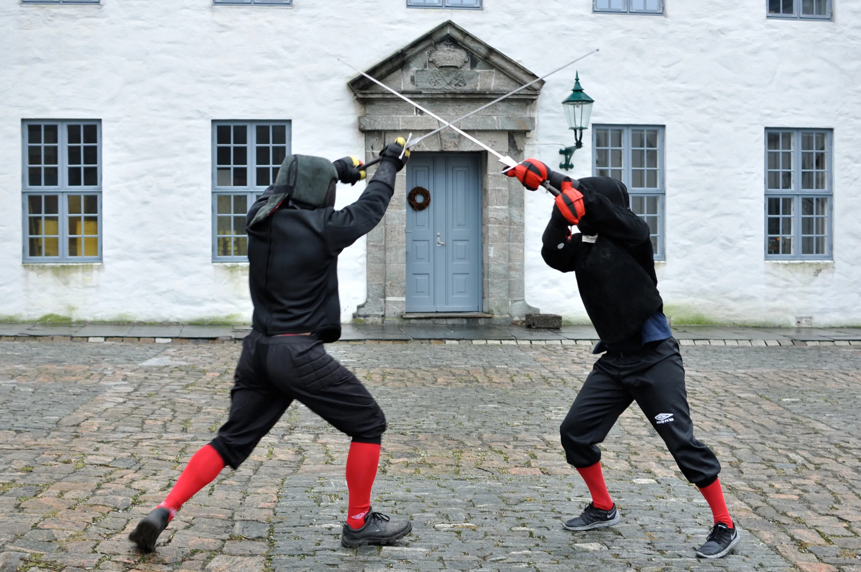 To fektere i svart beskyttelsesutstyr krysser langsverd foran en gammel blå dør på Bergenhus.