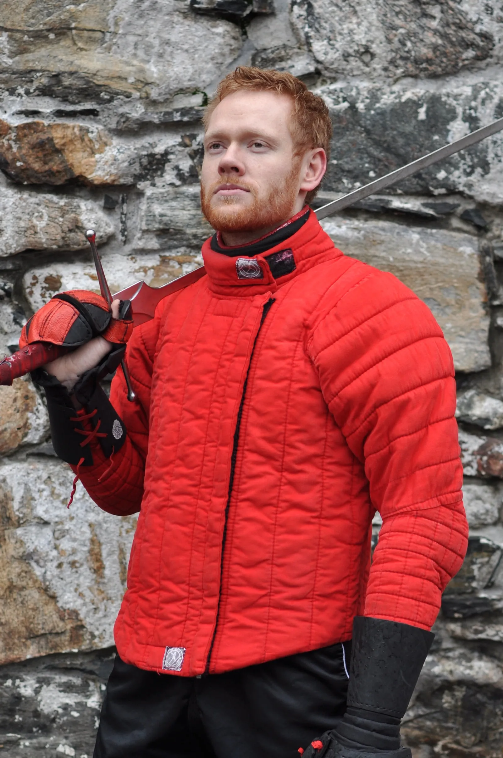 Fencer in a bright red fencing jacket with their mask tucked under one arm.