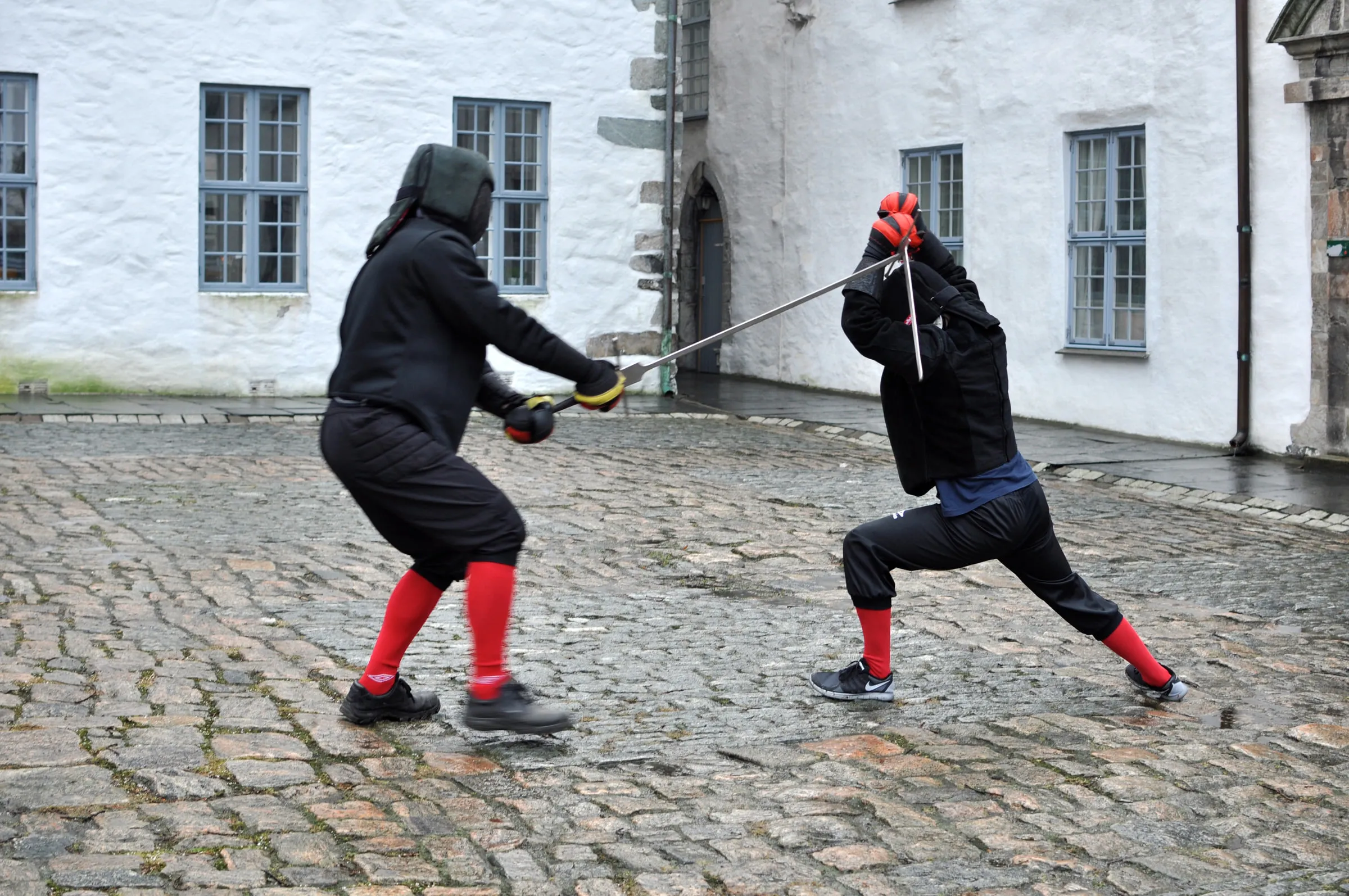 To fektere i sparring på brostein. Den ene går i utfall mens den andre parerer.